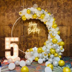 A beautiful 5th birthday setup with a white ring backdrop, a cascade of gold, white, and silver balloons, and a large light-up number '5'.