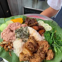 A generous, communal platter served on a large banana leaf, ready for sharing. This feast includes two types of rice, multiple pork preparations, fresh greens, and an assortment of vegetables.