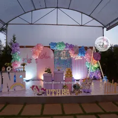 An outdoor unicorn-themed first birthday party. The setup features a large stage with pastel backdrops, a sequin wall, and of course, plenty of unicorns.