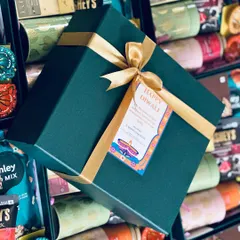 A close-up of our premium packaging for a Diwali hamper. The rich green box, lustrous gold ribbon, and custom-designed tag come together to create a feeling of luxury and celebration.