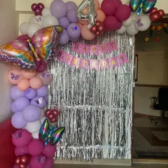 A fun butterfly theme for a 4th birthday, using a silver fringe curtain, a colorful balloon half-arch, and large butterfly foil balloons.