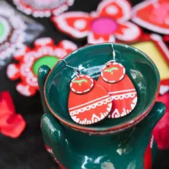 A close-up of vibrant, hand-painted wooden earrings, displayed in a quirky hand-shaped ceramic bowl.