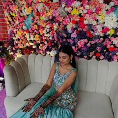A stunning bride seated against a wall of flowers, her mermaid-themed mehndi perfectly matching her enchanting look.