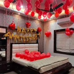 A classic romantic anniversary decoration for a bedroom. The room is filled with red balloons floating on the ceiling, with 'Happy Anniversary' foil letters placed above the headboard.