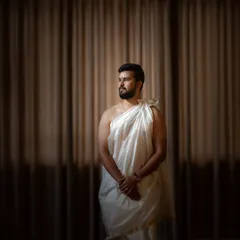 A classic portrait of the groom in traditional Brahmin wedding attire. The simple, elegant drapery and the soft, directional light create a powerful and dignified image.