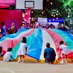 A large-scale parachute game in action during an outdoor sports day event. This activity involves dozens of children working together to create waves and play games, promoting large-group coordination.