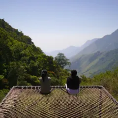 Two guests relaxing on a viewpoint net at my Munnar campsite, enjoying the incredible valley views.