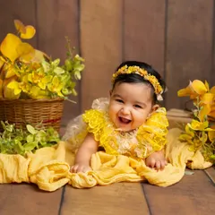 The most infectious giggle from a three-month-old during her milestone session. Lying on her tummy, she's surrounded by cheerful yellow flowers, creating a bright and happy scene.