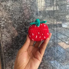 A view of the closed crochet strawberry AirPod case. The green top and white seed details make it look just like a real strawberry.