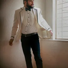 A full-body shot showing the complete tuxedo look, from the pleated shirt to the slim-fit trousers, creating a sleek silhouette.
