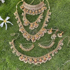 A full view of a temple jewellery set with pearl detailing, laid out on the grass. This shows the choker, two haarams, and the vaddanam.