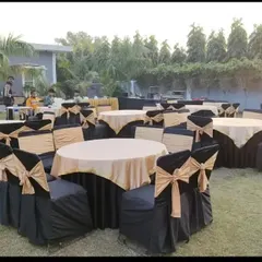 A simple and functional outdoor seating arrangement with round tables and black and gold chair covers, suitable for a large lunch or dinner event.
