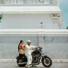 The groom, looking cool and confident in sunglasses, poses with his ride to the wedding, a classic motorcycle.