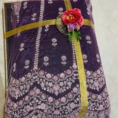 The details make all the difference. This close-up shows a richly embroidered purple fabric, perfect for a bridal lehenga, secured with a simple gold ribbon and a delicate floral accent to complement its intricate design.
