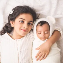 A tender moment between a big sister and her newborn sibling. This simple, classic studio shot focuses on the beginning of a lifelong bond, a precious memory for any growing family.
