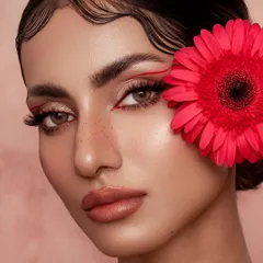 This angle offers a different perspective on the graphic liner and floral theme. The model's gaze is directed towards the viewer, creating a more intimate connection while still showcasing the artistic makeup and flawless, glowing skin.