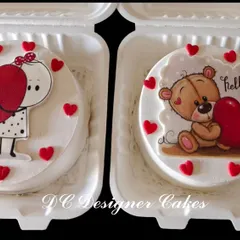 A pair of adorable bento cakes perfect for Valentine's Day or an anniversary. These mini cakes feature cute, hand-drawn style characters holding hearts, all packed in individual boxes.