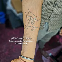 This line art tattoo shows a parent's hand holding a child's, with "Mom Dad" written below. It's a simple yet powerful design symbolizing family bonds.