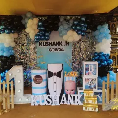 A fun Boss Baby themed first birthday setup with a sequin backdrop, a blue, black, and white balloon arch, and character-inspired props.