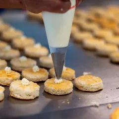A close-up of our pastry team at work. A chef pipes delicate swirls of cream onto freshly baked scones, a small but crucial detail for an unforgettable high tea experience.