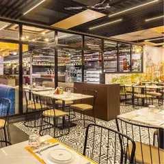 This section of the restaurant features striking black and white patterned floor tiles that contrast with the warm wood tones and simple metal chairs. A glass partition provides a view of the well-stocked bar area, adding to the open feel.