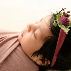 A close-up profile of a sleeping newborn, focusing on their soft skin and the texture of the floral headband.