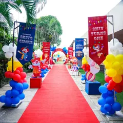 A grand red carpet entrance lined with colorful banners, balloons, and clown cutouts, leading guests into the circus celebration.