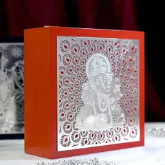 This vibrant orange gift box is adorned with a silver-plated Ganesha motif, surrounded by a delicate peacock feather pattern. It is a luxurious and auspicious choice for any celebration.