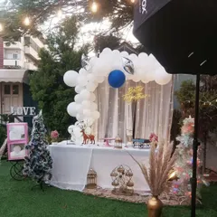 A winter-themed "Better Together" backdrop. This setup combines a white balloon arch with festive elements like iridescent Christmas trees, a reindeer figure, and a sheer curtain with fairy lights.