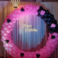A modern pink and black circular balloon backdrop with a "Happy Birthday" sign, perfect for a stylish party.