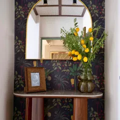 A stylish foyer corner featuring a bold, dark tropical wallpaper. We added a custom-designed console table and an arched mirror to create a welcoming and dramatic first impression.