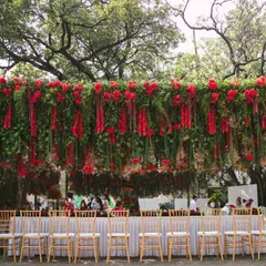 A wider perspective of the hanging red wisteria installation over a long dining table. This setup demonstrates how we can use vertical space to make a bold statement, even in an open-air setting, ensuring the decor is a central feature of the event.