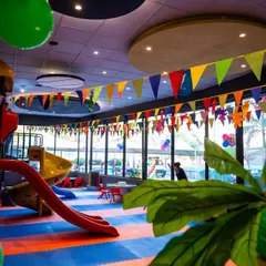 A wide view of our indoor play area, decorated with colorful banners for a celebration. You can see the large slide, climbing structures, and open space for running and playing.
