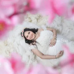 Dreaming of the little one. This creative shot, framed by soft pink flowers, captures the mother-to-be in a moment of serene contemplation, looking absolutely angelic in a white ruffled dress.