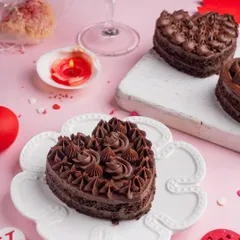 A rich, heart-shaped chocolate cake, perfect for a decadent Valentine's treat. The moody lighting and single red candle create an intimate and romantic vibe.