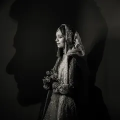 A powerful and creative silhouette portrait. The bride stands illuminated against a dark wall that bears the shadow of her groom's profile, symbolizing their deep and ever-present connection.