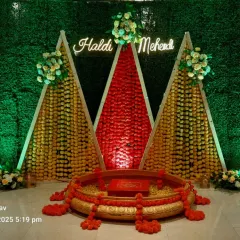This is a vibrant Haldi and Mehendi stage I created. It uses a traditional green grass wall backdrop with geometric structures made of marigold flowers and a custom neon sign, perfect for pre-wedding ceremonies.