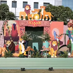 The main stage for a 'Lion King' themed birthday party, featuring a massive backdrop with all the beloved characters from the Pride Lands. The setup includes animal props and balloon garlands in earthy tones.