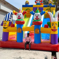 A large, joker-themed bouncy castle with multiple slides and clown figures. One of our team members is sitting in front to give a sense of its large scale.