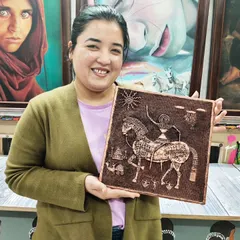 A student with her intricate relief artwork depicting a traditional Indian horse motif. This technique involves building up layers of clay to create a raised design.