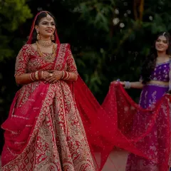 A stunning bridal portrait capturing the bride in her magnificent red lehenga. The bridesmaid attending to her veil adds a touch of story to this elegant shot.