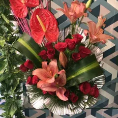 A modern table arrangement featuring exotic anthurium flowers, red roses, and lilies. This style is perfect for corporate offices or as a contemporary home decoration.