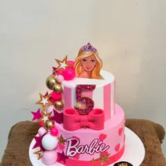 A perfect cake for a Barbie fan's 5th birthday. This two-tiered design combines pink stripes, polka dots, and a large fondant bow, topped with a Barbie figurine and sparkling stars for a glamorous party theme.