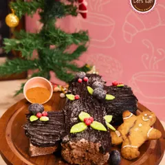 A classic Christmas Yule Log, decorated to resemble a festive log with chocolate bark, meringue mushrooms, and holly. It's a stunning and delicious addition to your Christmas table.