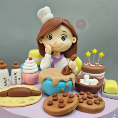 A close-up of the baker girl figurine, surrounded by tiny, handcrafted baking ingredients like salt, sugar, cookies, and a rolling pin.