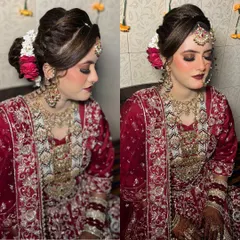 A closer look at the bridal hairstyle my team created. This elegant updo is adorned with fresh red and white flowers, perfectly complementing her maroon outfit and adding a touch of softness to the overall regal look.