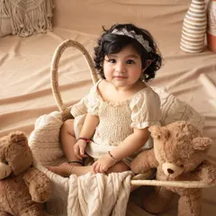 A beautiful one-year-old girl in a neutral-toned outfit, sitting in a basket with her teddy bears. A classic and simple first birthday portrait.