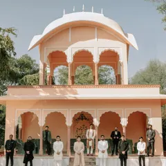 The groom's party, dressed in traditional attire, posing in front of a historic Rajasthani building, capturing the essence of a destination wedding.