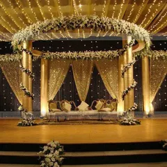 I am very proud of this glamorous reception stage. The design uses a gold and white color palette, with a stunning floral arch, sparkling drapes, and fairy lights to create a truly magical and celebratory space.