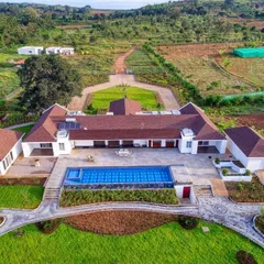 An aerial view of a sprawling farmhouse we designed by the backwaters of Kabini. The architecture is planned for symmetrical elegance, integrating the residence, infinity pool, and extensive landscaping into a cohesive, luxurious estate.